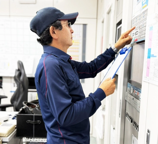 K.H.さん仕事風景　バインダーを手にモニター機器の点検・操作