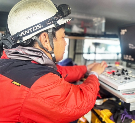 G.D.さん仕事風景　作業車内で点検用モニターと操作パネルに向かい、真剣な眼差しで機械操作